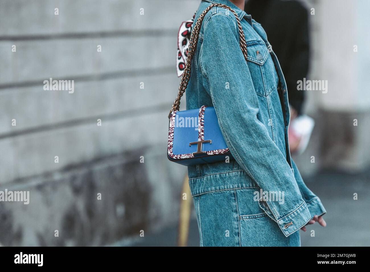 Milan, Italy - February 25, 2022: Crop anonymous female in denim outfit with blue Tod's handbag with chain walking on street. Stock Photo
