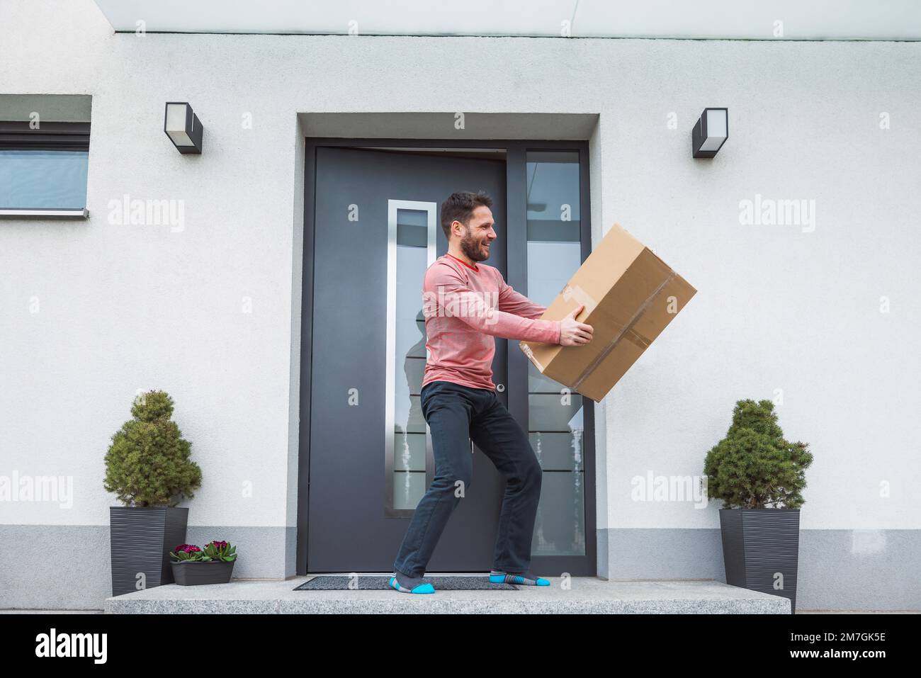 Thrilled man holding a big cardboard box that just came in the mail while standing outside the front door Stock Photo
