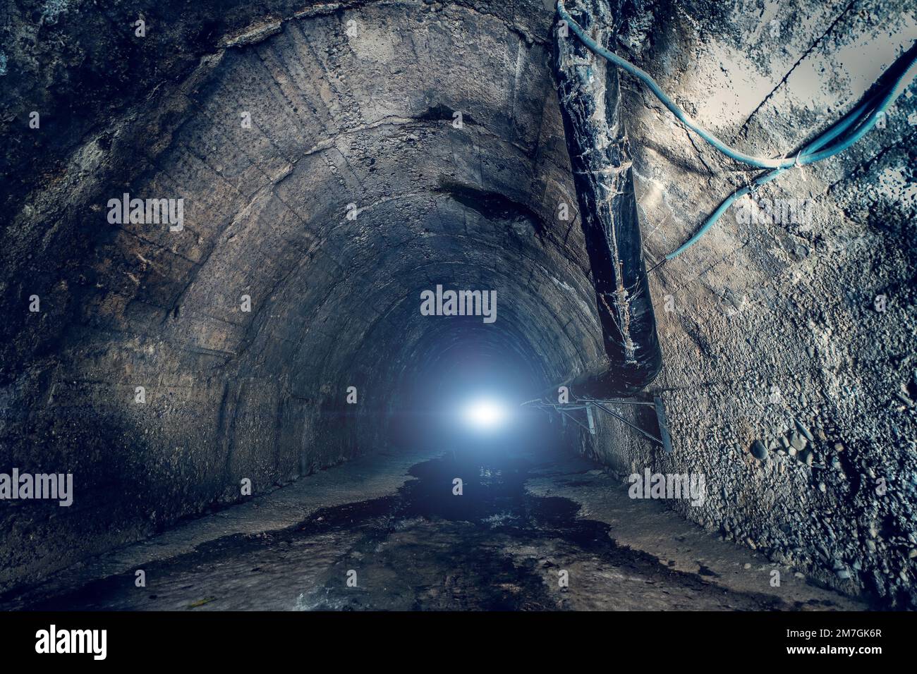 Sewer water in big underground sewage tunnel. Inside dark urban sewerage corridor tunnel with light in end. Stock Photo