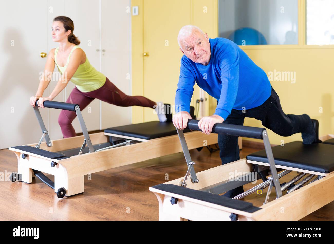 Elderly man performing pilates exercises on reformer during group