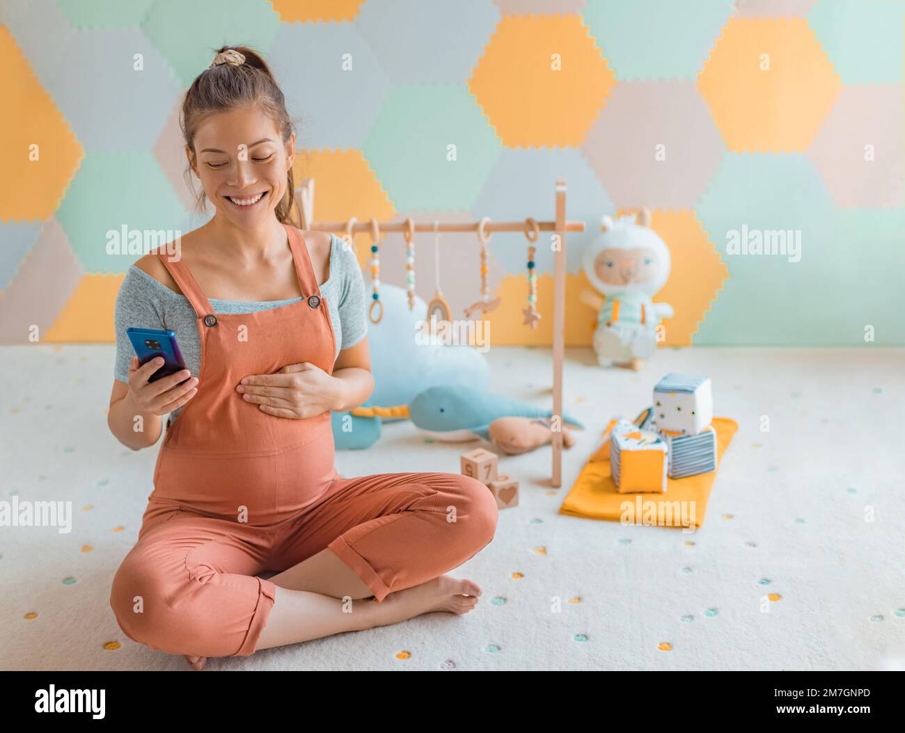 Pregnant woman belly in nursery playrooom using phone app for online shopping maternity clothing or reading about labor and birth. Pregnancy concept Stock Photo
