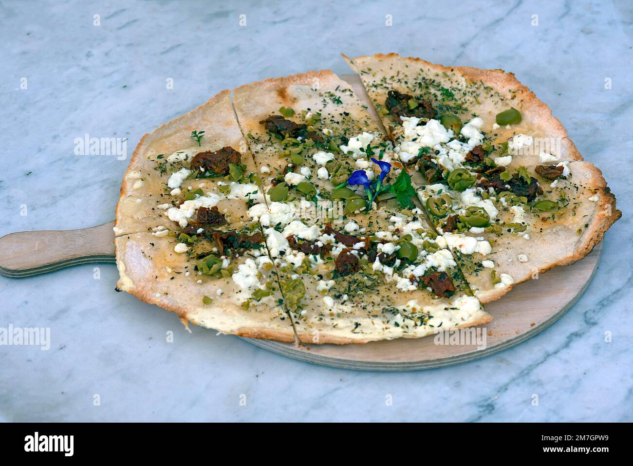 Flammkuchen with olives dried tomatoes and feta cheese on a wooden board, Bavaria, Germany Stock Photo