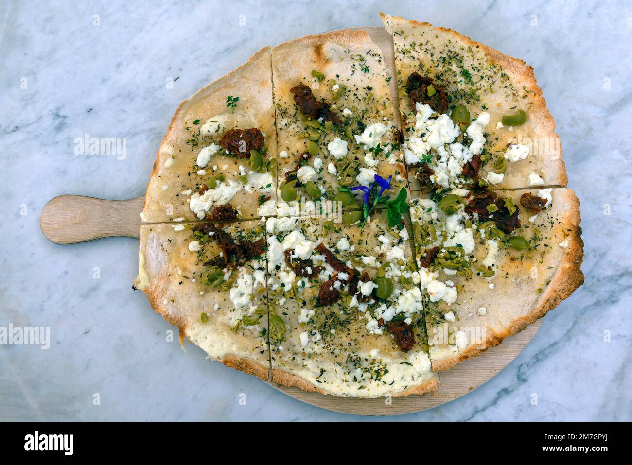 Flammkuchen with olives dried tomatoes and feta cheese on a wooden board, Bavaria, Germany Stock Photo