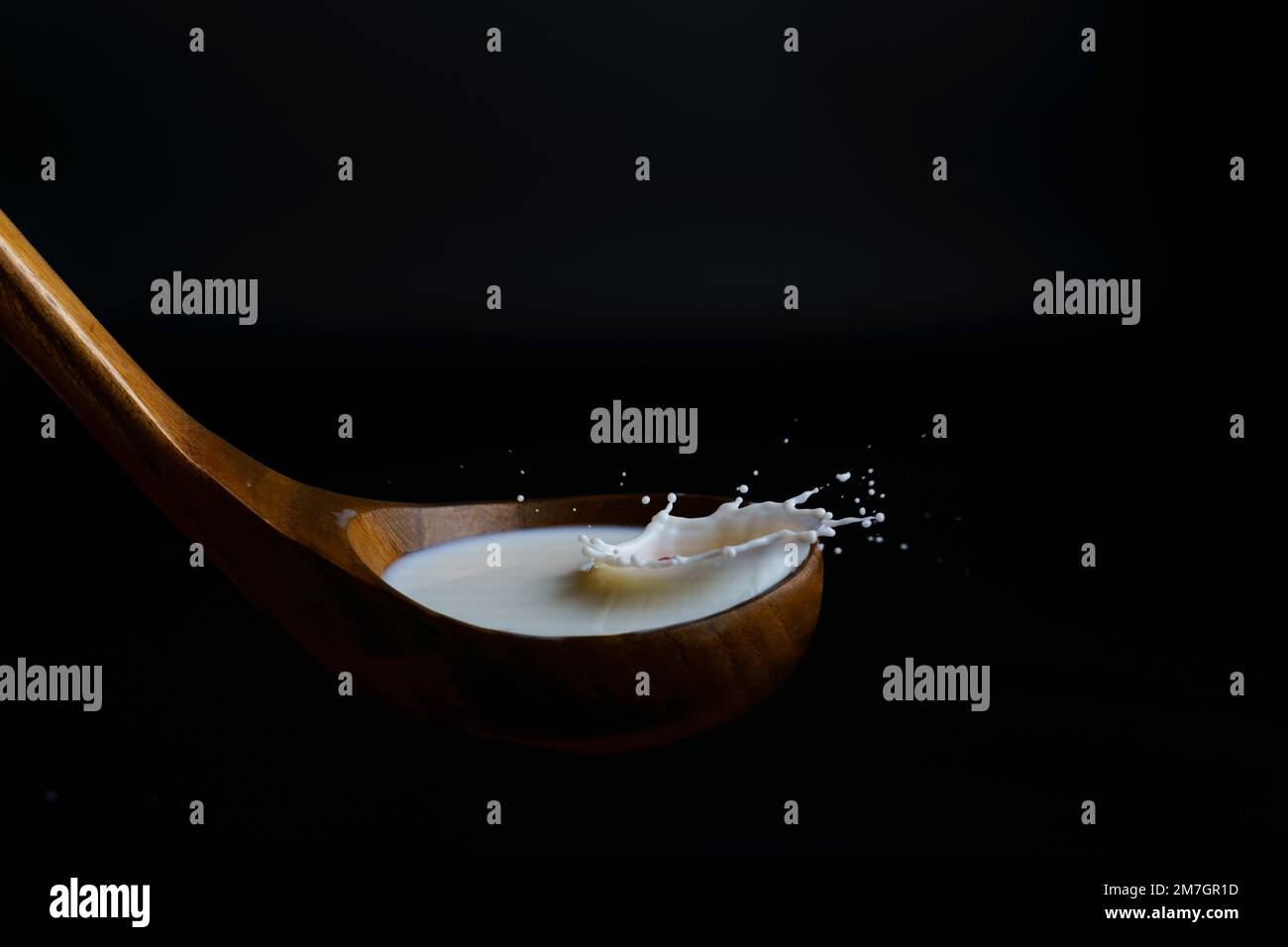 Milk splashing on a wooden ladle, with splash effect and black background Stock Photo
