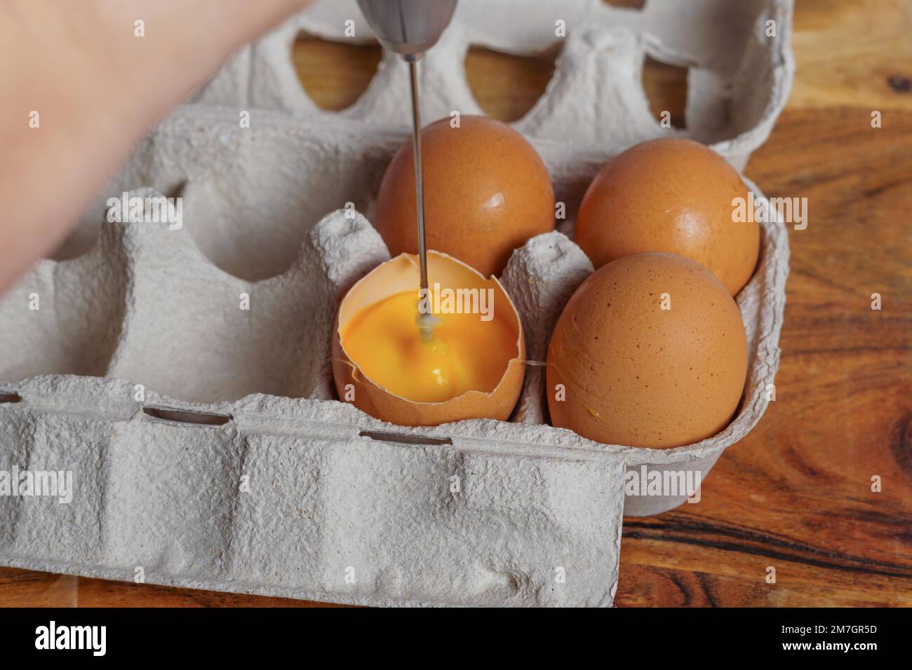 Woman beating an egg in its own shell with a small blender, several