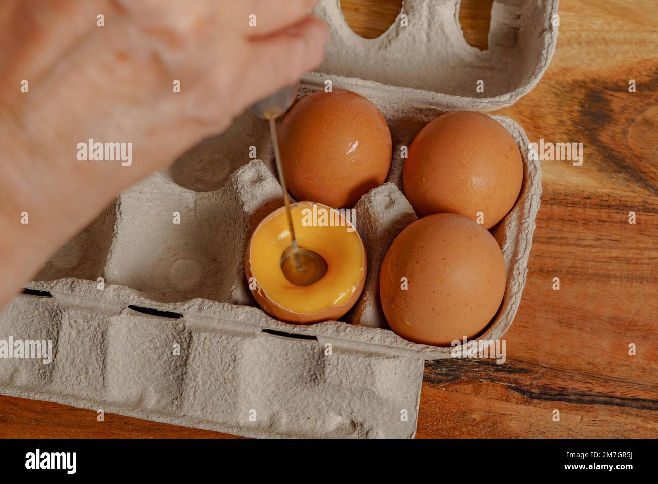 Woman beating an egg in its own shell with a small blender, several