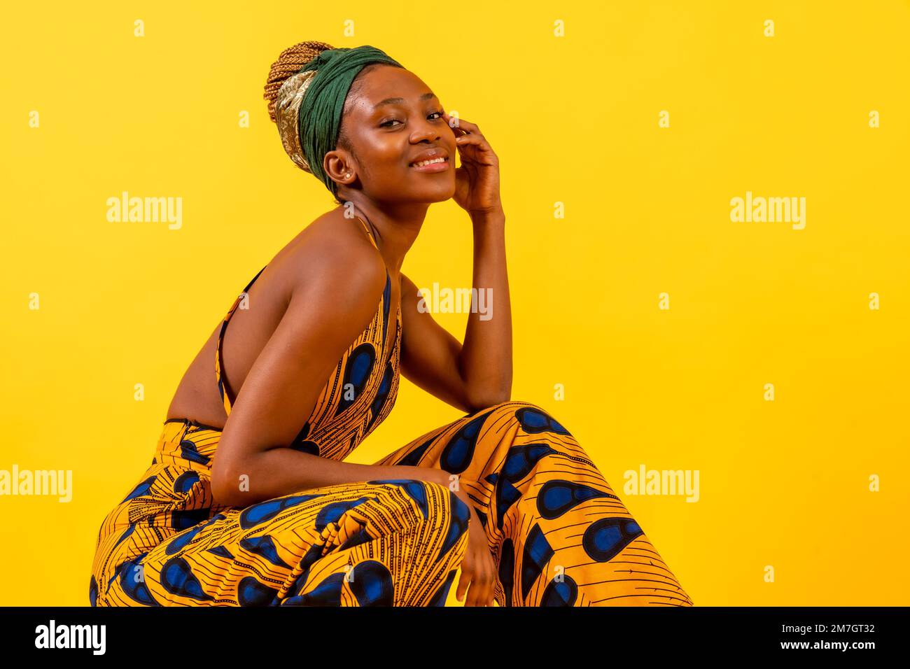 One person woman of black ethnicity with traditional costume on yellow background, sitting smiling Stock Photo