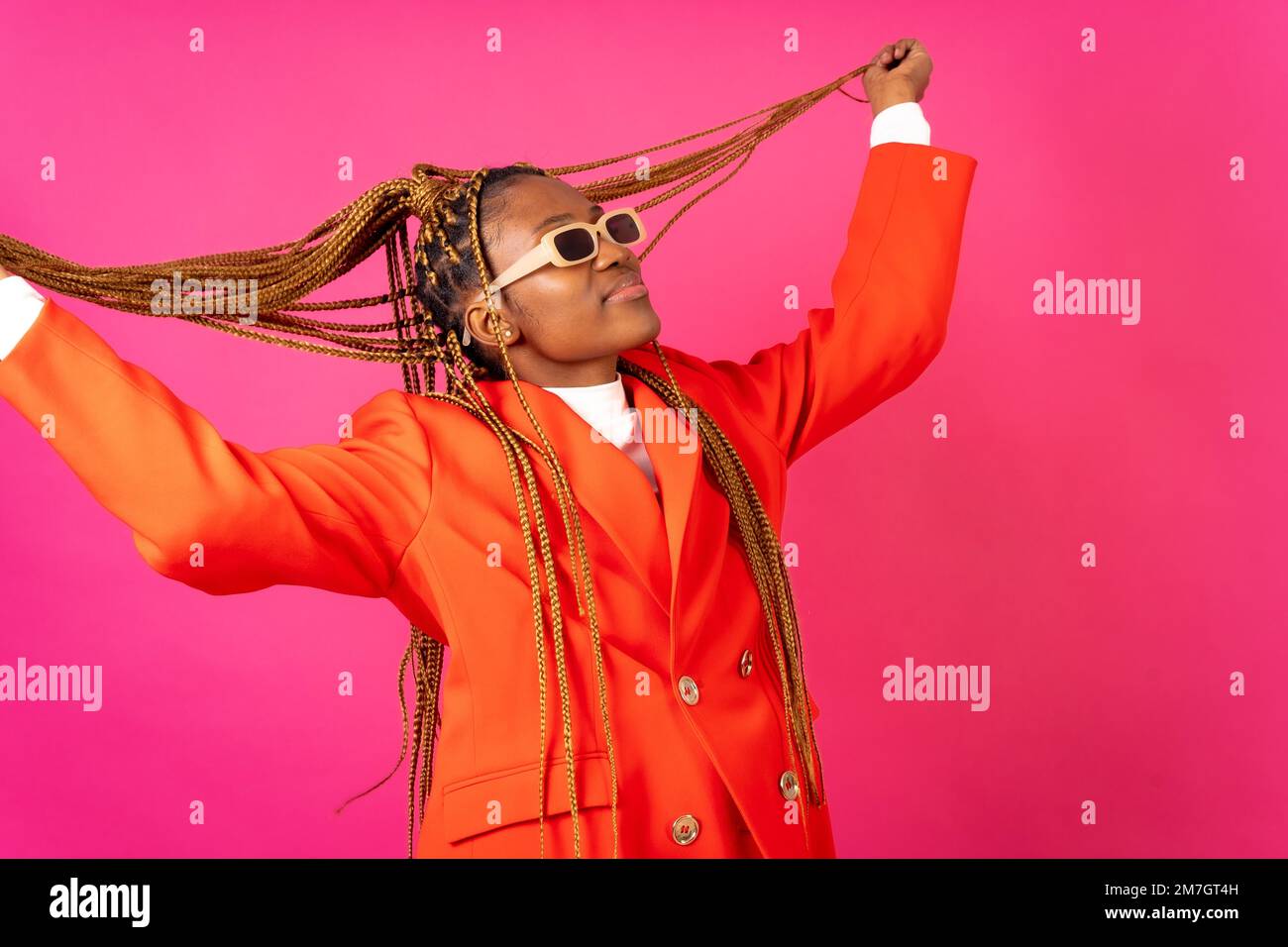 African young woman with braids on a pink background, in a red suit having fun and dancing Stock Photo