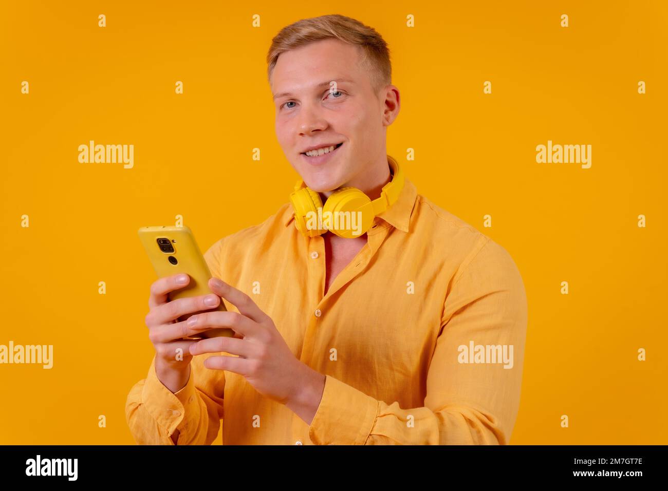 Young blond caucasian man on a yellow background, selecting the music on the mobile Stock Photo
