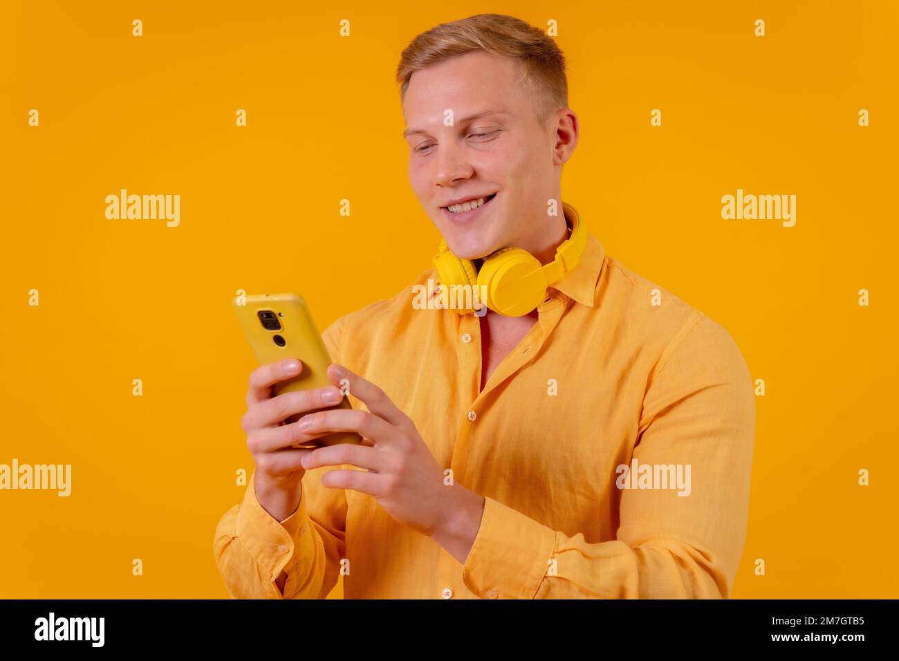 Young blond caucasian man on a yellow background, selecting the music on the mobile Stock Photo