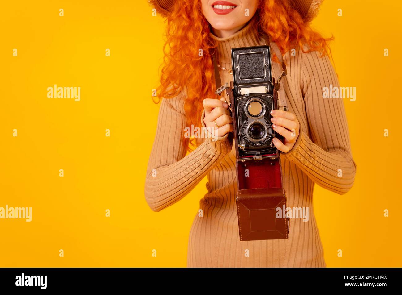 Unrecognizable redhead on a yellow background, copy space, with a vintage photo camera Stock Photo