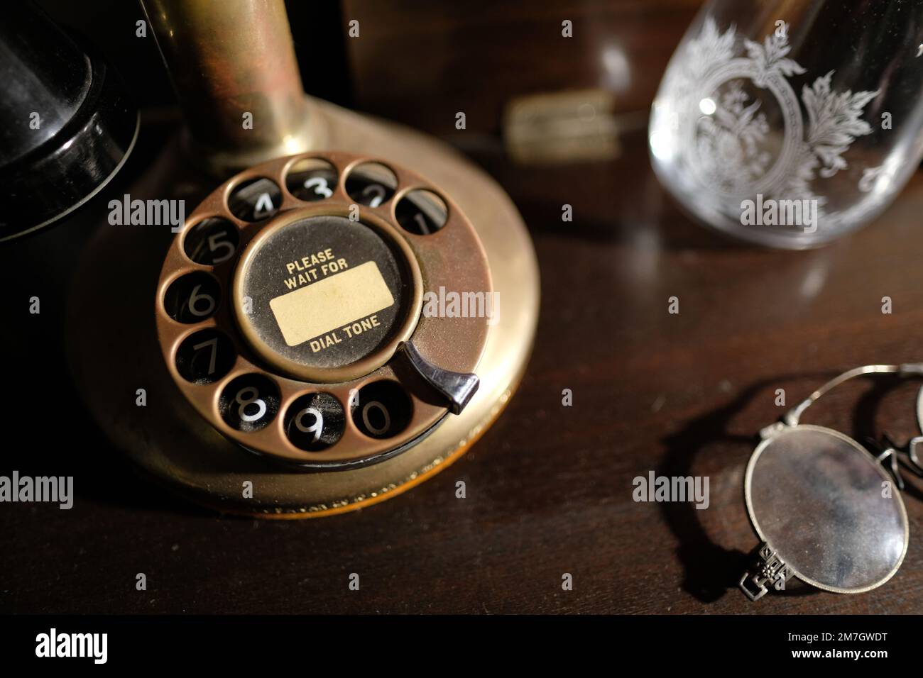 Base of an early 1900s Western Electric Brass Bullnose Candlestick Rotary Dial Telephone with Please Wait for Dial Tone script on number's dial. Stock Photo