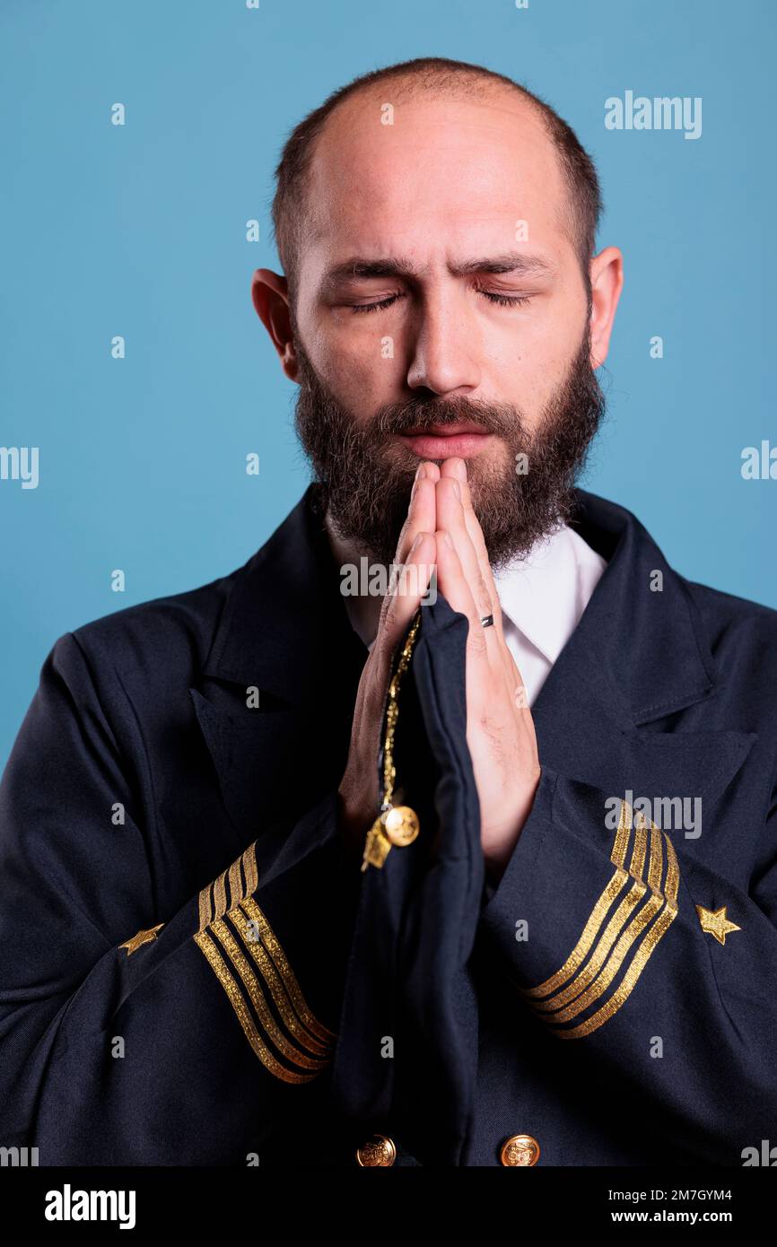 Airline pilot in uniform praying to gods with closed eyes, standing