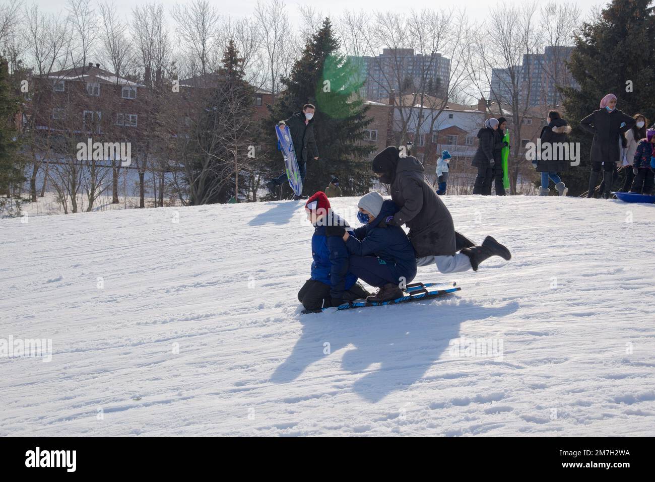 Toronto, Ontario / Canada - 02/21/2022: Family playing toboggan in winter. Outdoor winter landscape. Stock Photo