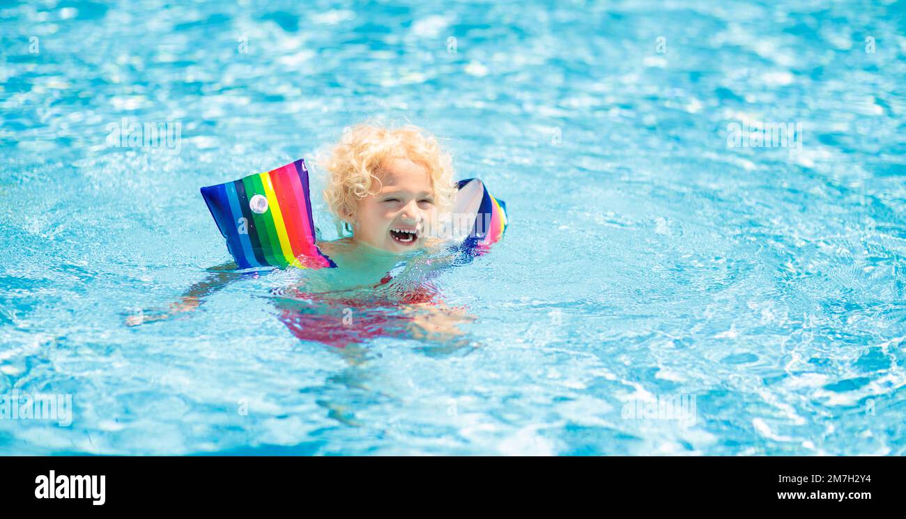 Child in swimming pool wearing colorful inflatable armbands. Kids learn