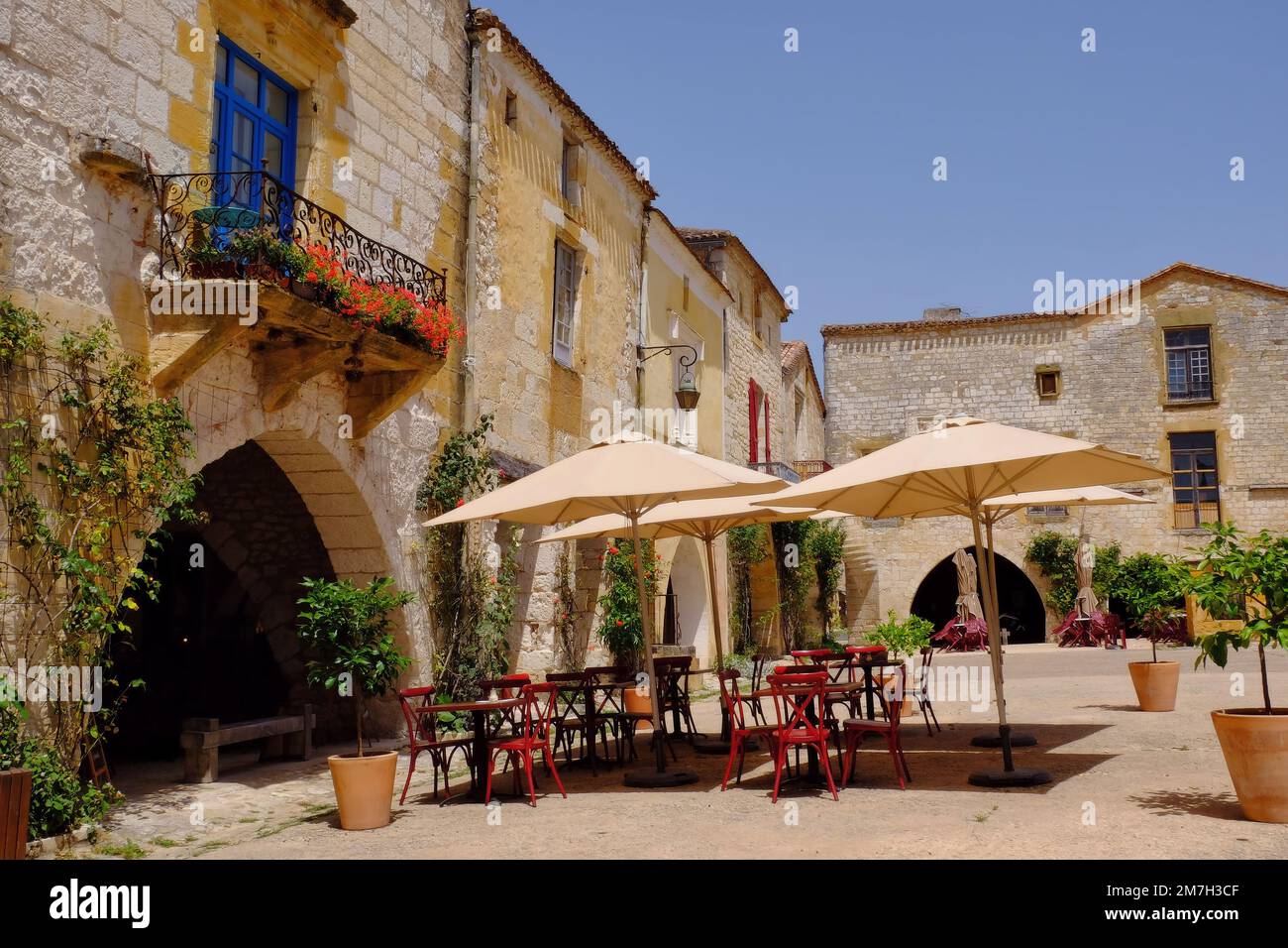 Monpazier: Colourful buildings and restaurants with flowers and umbrellas in square of bastide town of Monpazier, Dordogne, Aquitaine, France Stock Photo