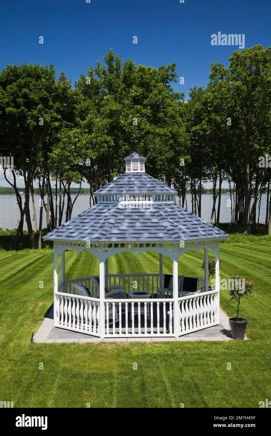 White wooden gazebo with blue and grey nuanced asphalt shingles roof in landscaped backyard in