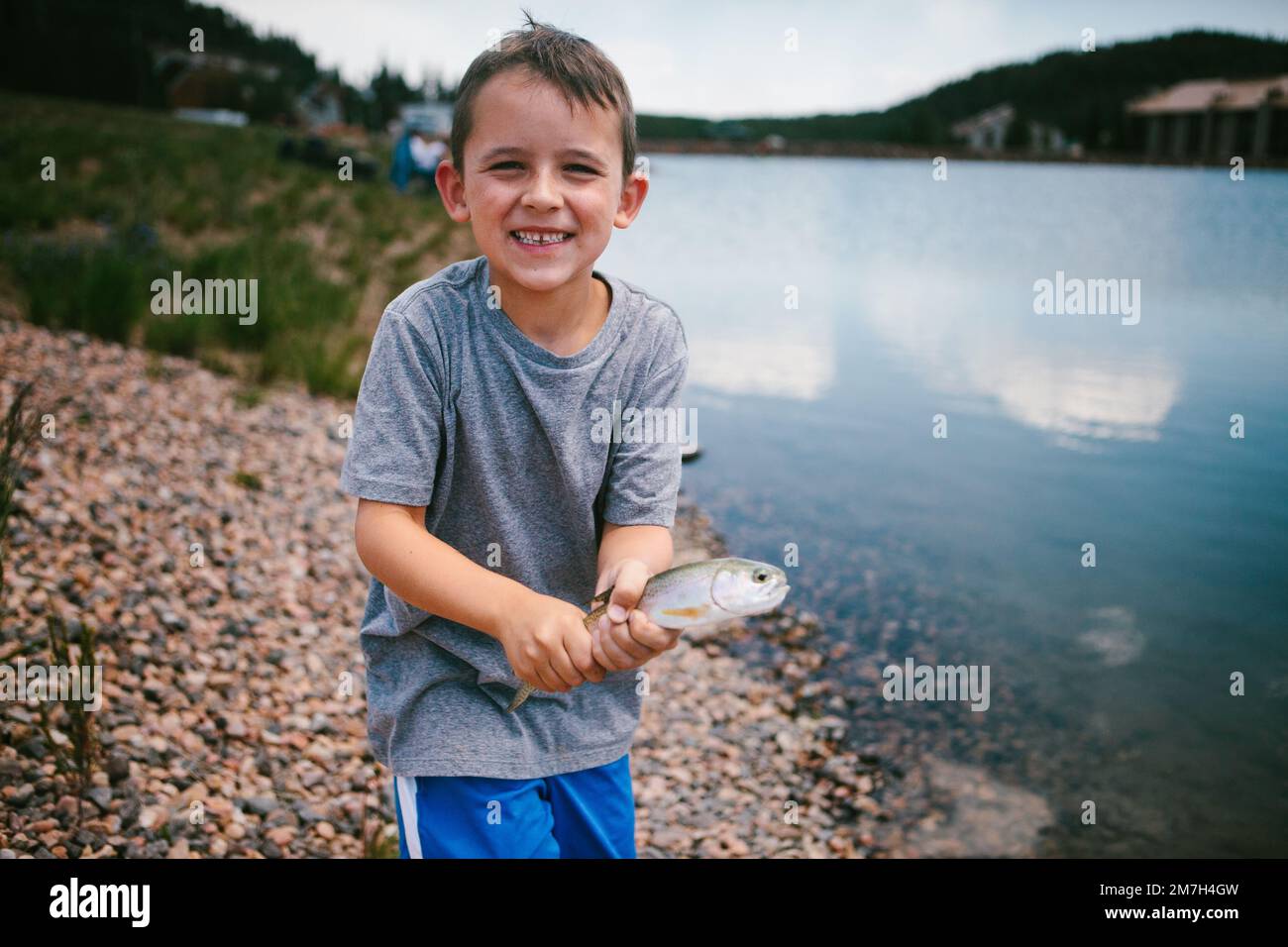 Boy smiles with fish he caught in mountain lake on vacation Stock Photo