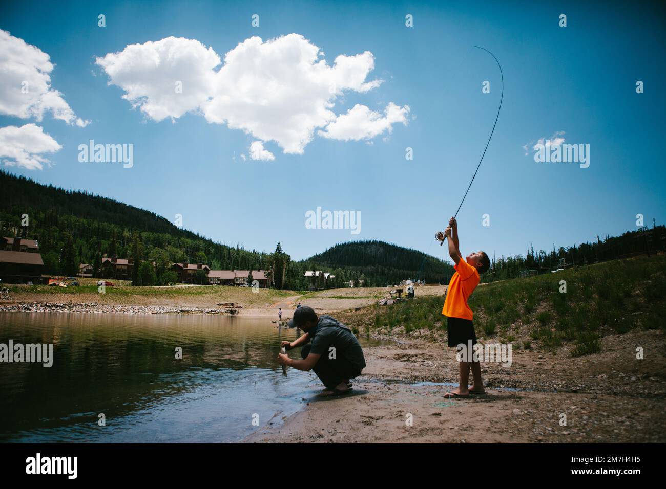 Boy catches fish from lake in mountain on vacation with dad Stock Photo