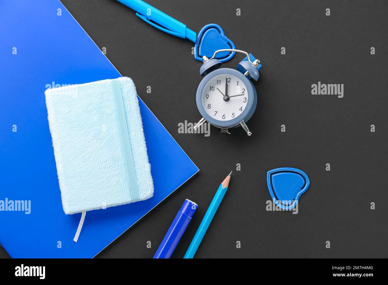 Set of blue stationery with notebooks and alarm clock on dark ...