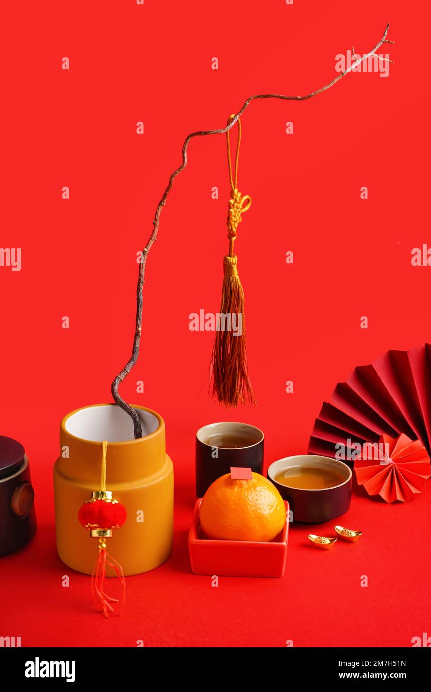 Cups of tea, mandarin, vase with tree branch and Chinese symbols on red