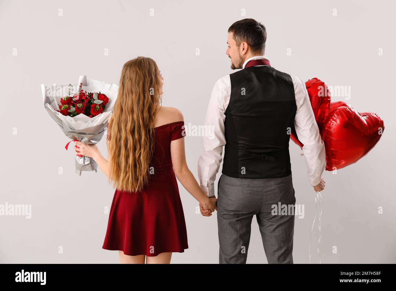 Happy young couple with heart-shaped balloons and flowers on light ...