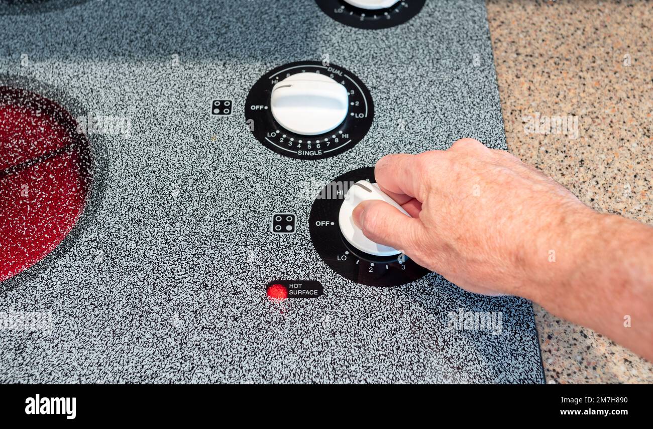 Male hand turning temperature control dial on stove top oven cooking