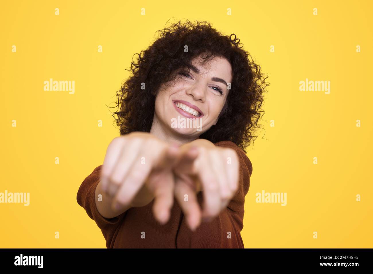 Young brunette woman pointing to you and the camera with fingers, smiling positive and cheerful female isolated over yellow background. Stock Photo