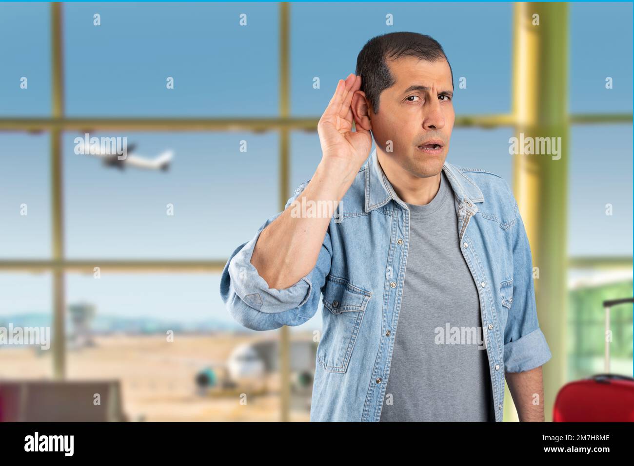 Studio shot of a handsome  man with at airport smiling with hand over ear listening and hearing to rumor or gossip. Deafness concept. Stock Photo