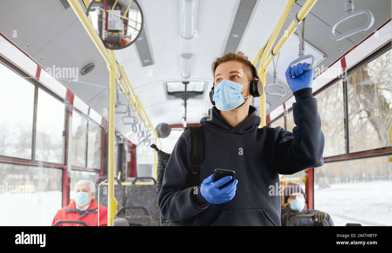Front view of crowd of people traveling by bus, wering medical masks and gloves during global pandemic. Young man standing on pubic transport, paying. Concept of coronavirus. Stock Photo