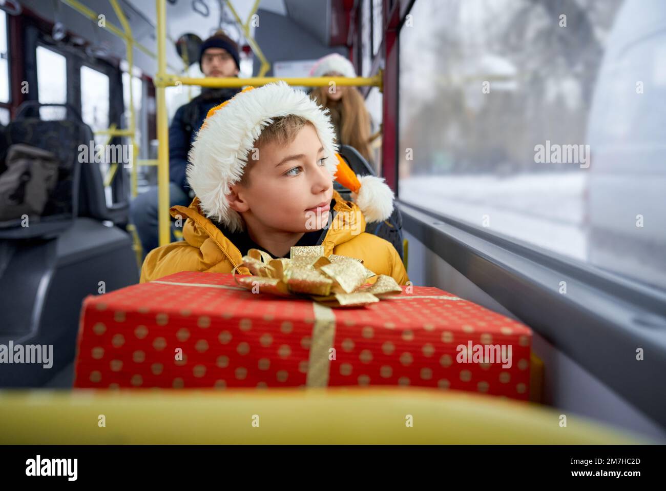 Front view of passengers traveling by means of public transport druring winter, Christmas holidays. Boy sitting, holding present, looking through window. Concept of winter. Stock Photo