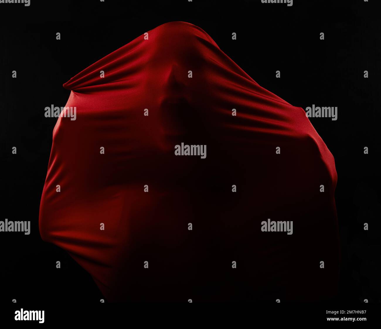 Trapped by fear. Human figures trapped in red fabric and struggling to break free while isolated on black. Stock Photo