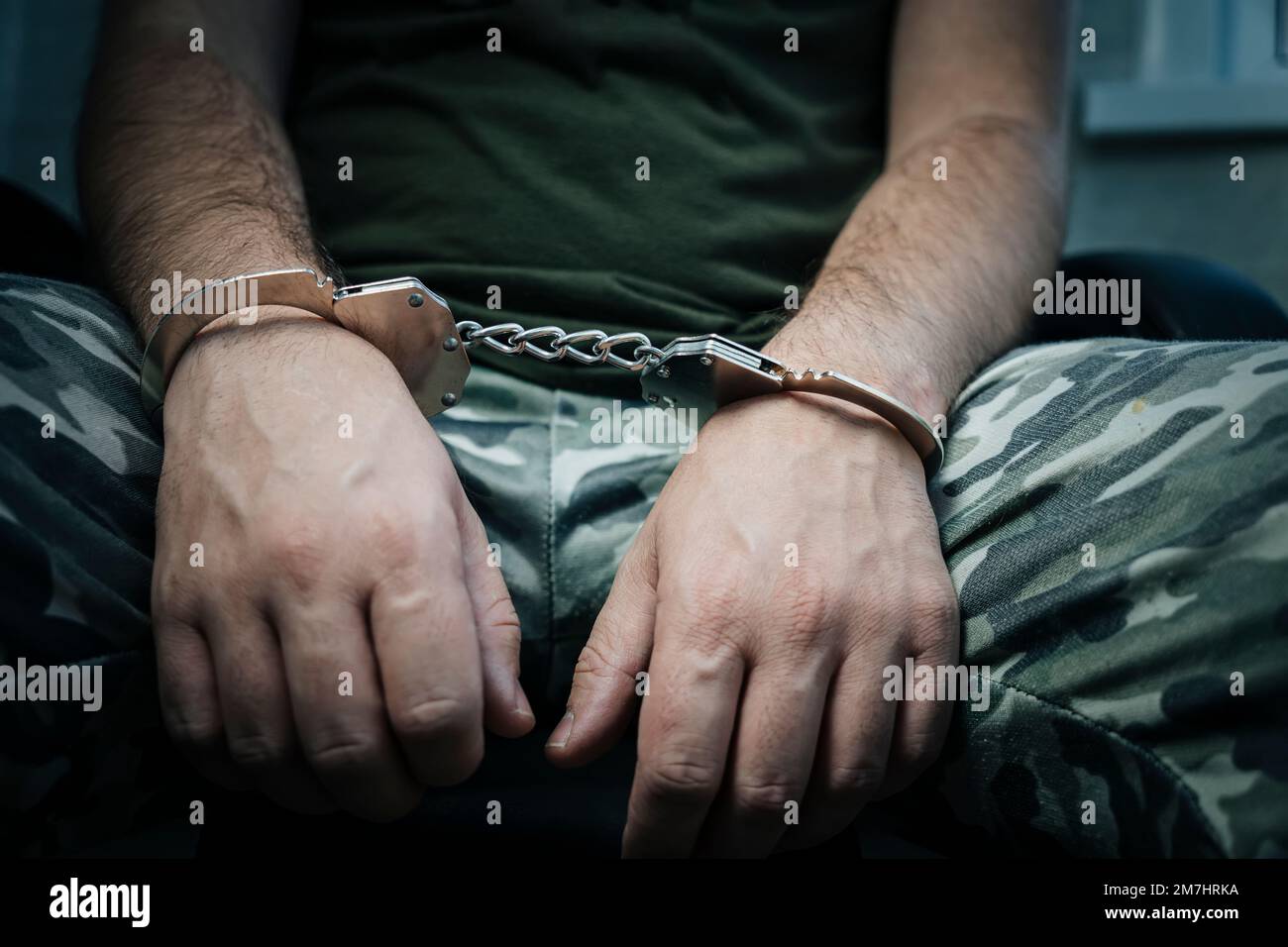military soldier in handcuffs, hands behind his back, on a dark background. Concept: war criminal, prisoner of war, tribunal. a prisoner of war under Stock Photo