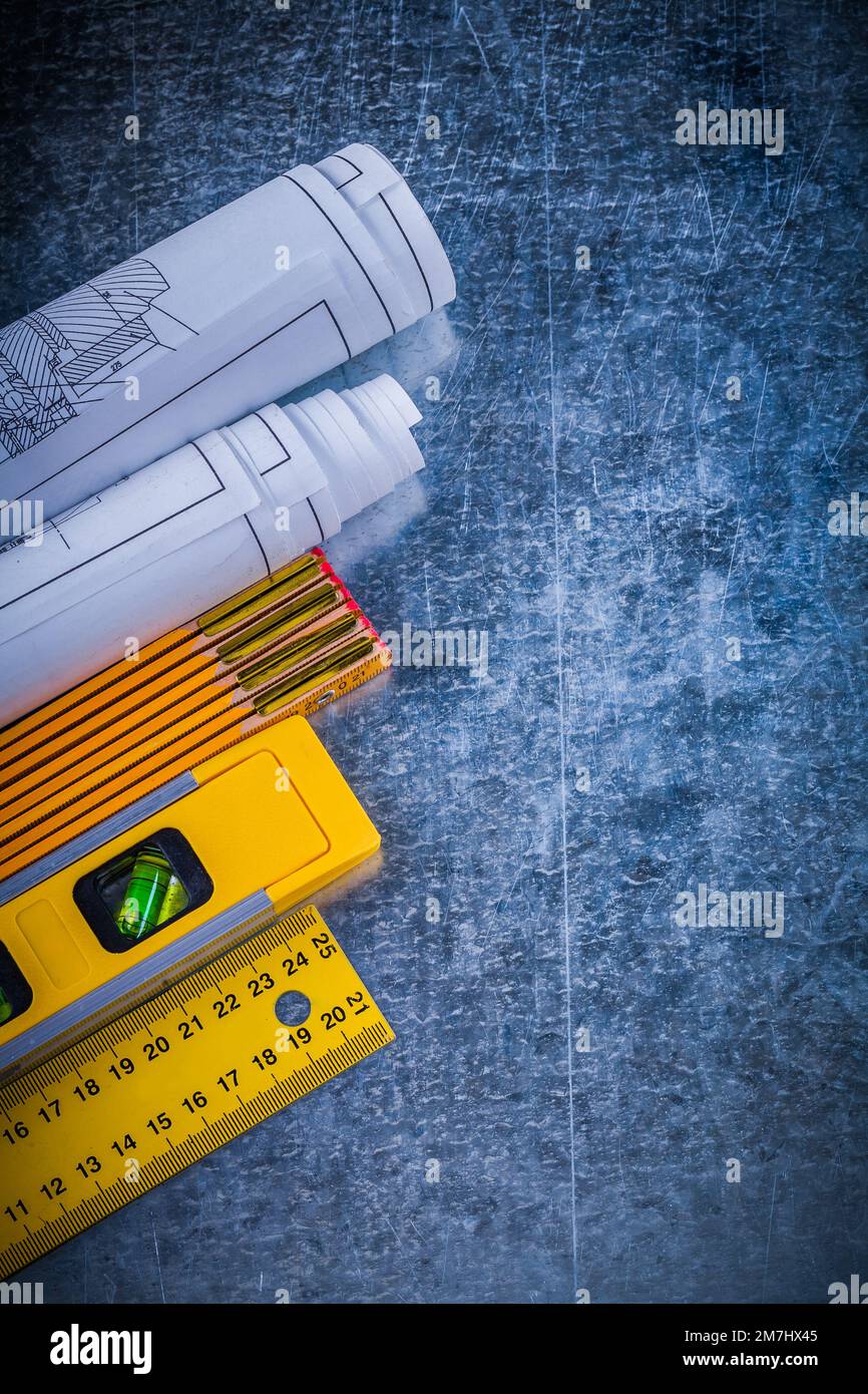 Blueprints yellow ruler construction level and wooden meter on metallic scratched background vertical view maintenance concept. Stock Photo