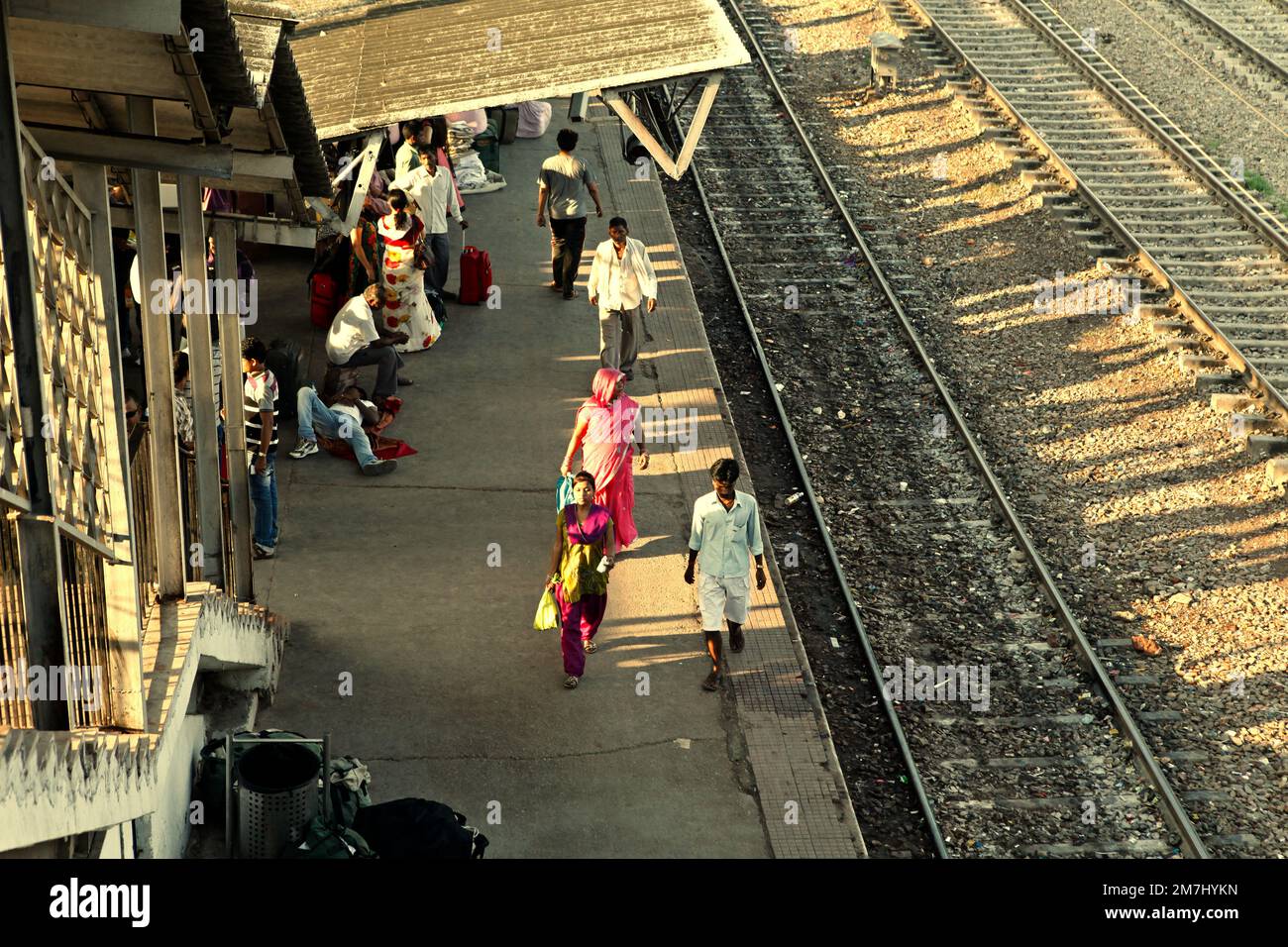 Train passengers are walking on passenger platform, on the side of railroad tracks at New Delhi Railway Station in Delhi, India. Stock Photo