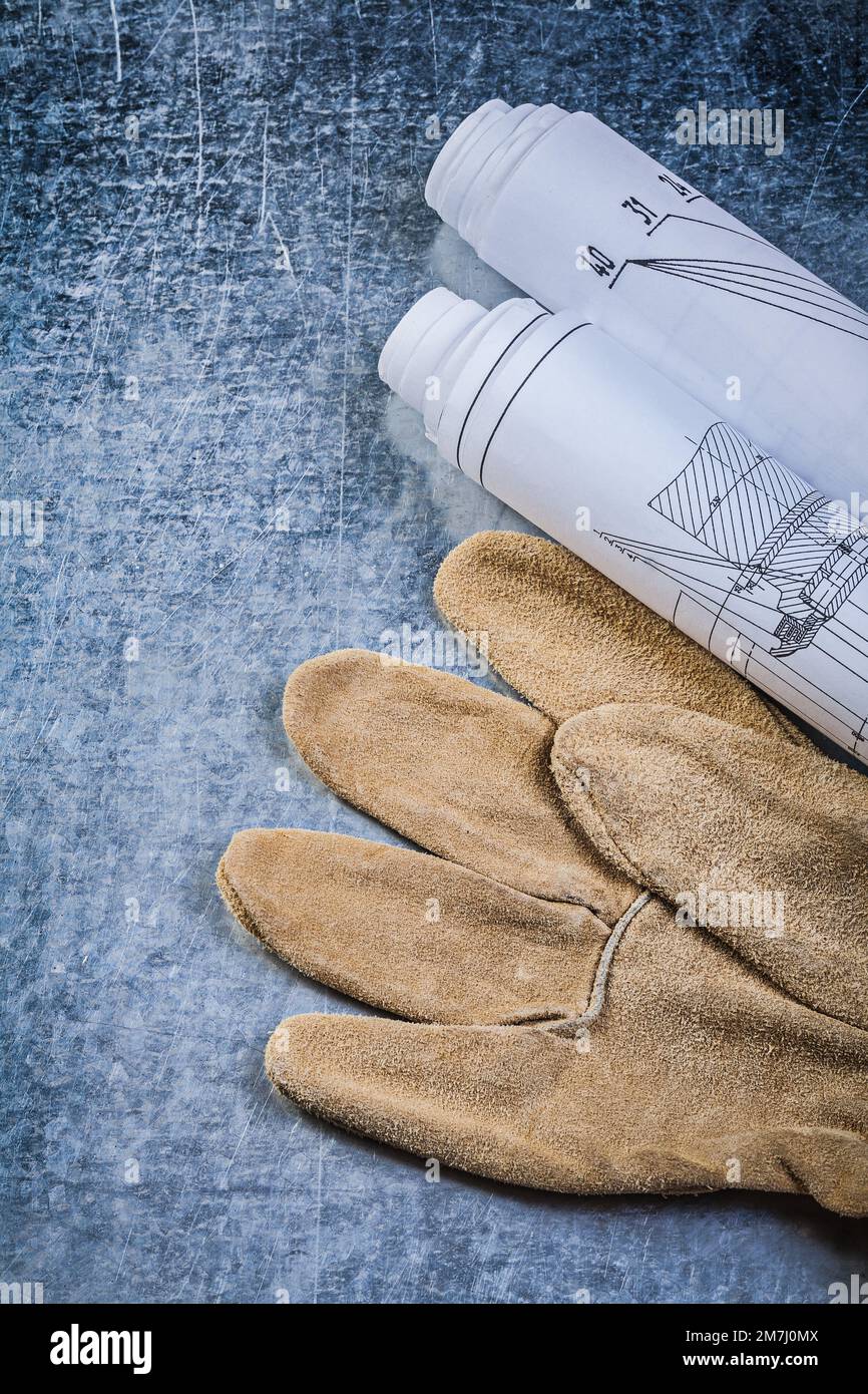 Rolled construction drawings leather safety gloves on metallic background top view. Stock Photo