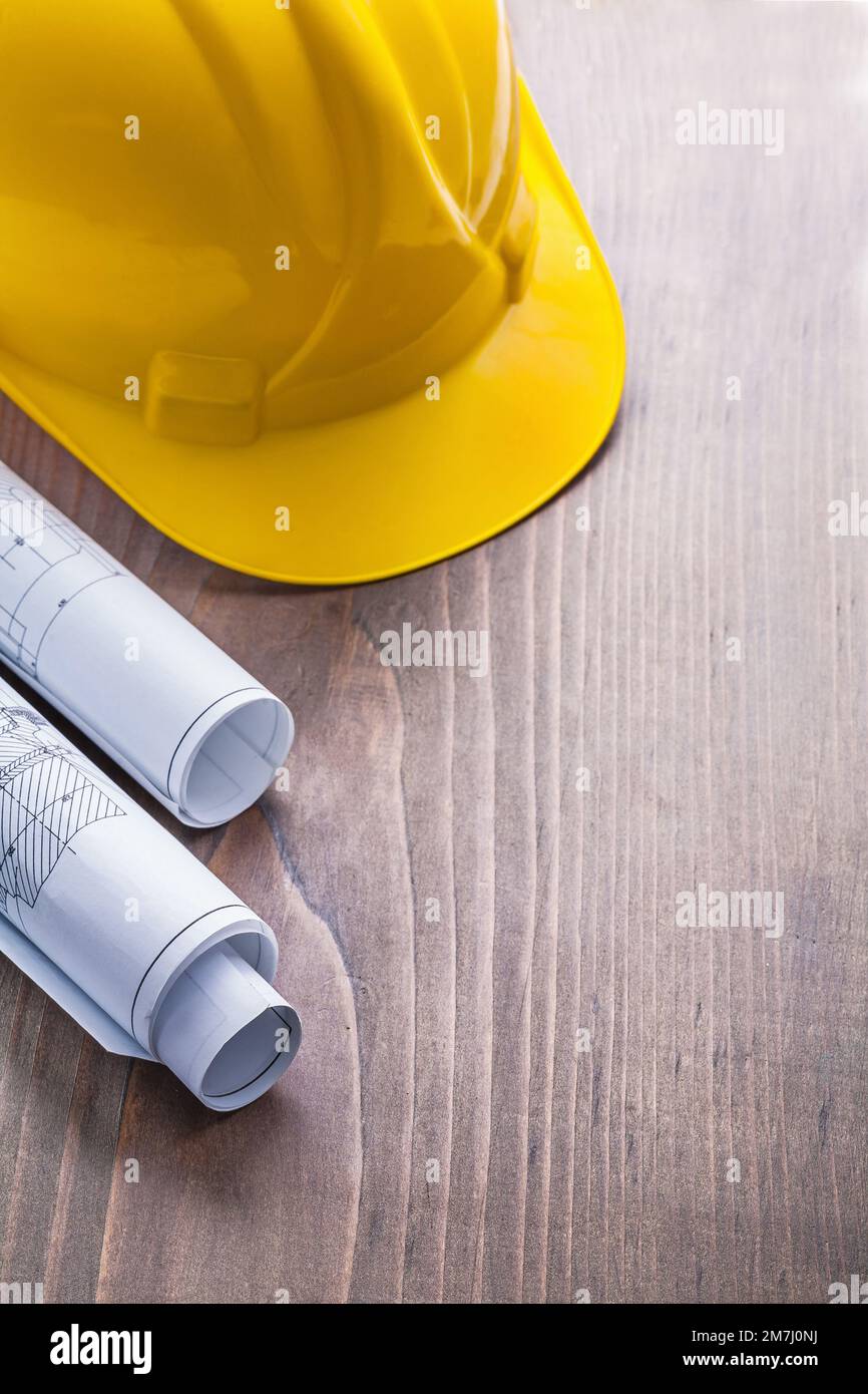 rolled blueprints and yellow helmet on vintage wooden board with ...
