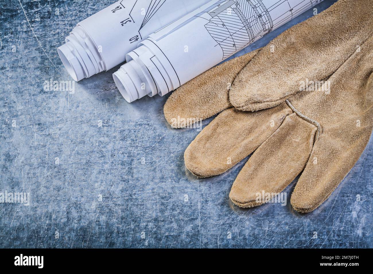 Rolled engineering drawings leather safety gloves on metallic background construction concept. Stock Photo