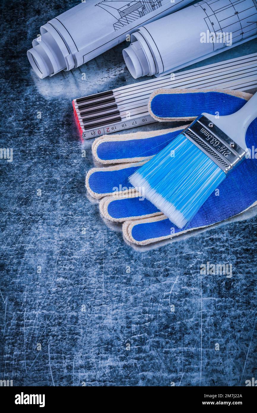 Wooden meter paintbrush safety gloves and rolled blueprints vertical ...