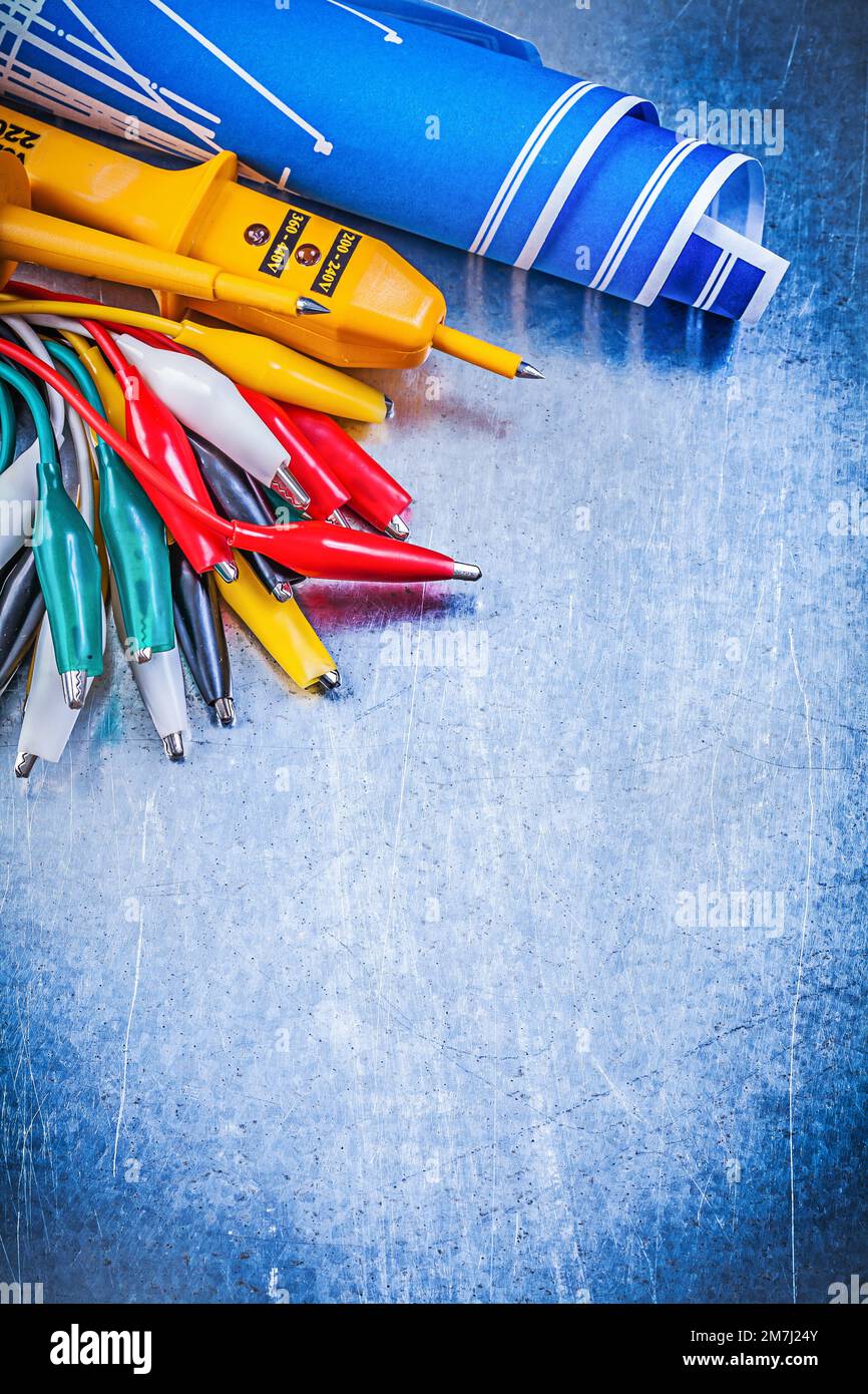 Yellow electrical tester crocodile cables set blue construction drawings on metallic background electricity concept. Stock Photo