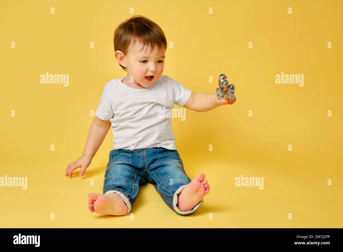 Toddler baby plays with a musical rattle bells on a stick, studio