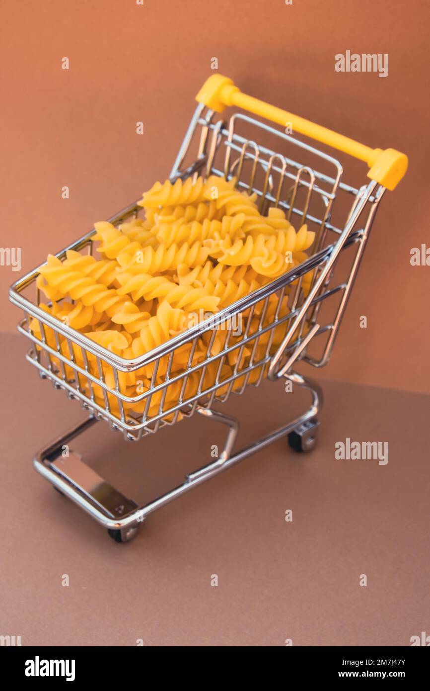 Shopping trolley cart Filled With Pasta on Beige background. Copy space