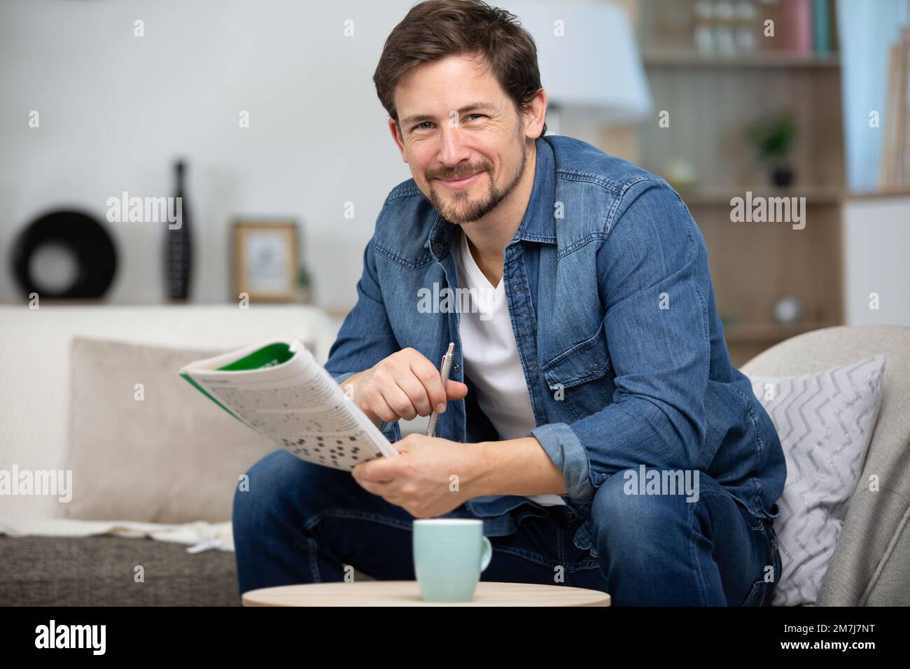 man sitting on sofa and doing crossword puzzle in newspaper Stock Photo