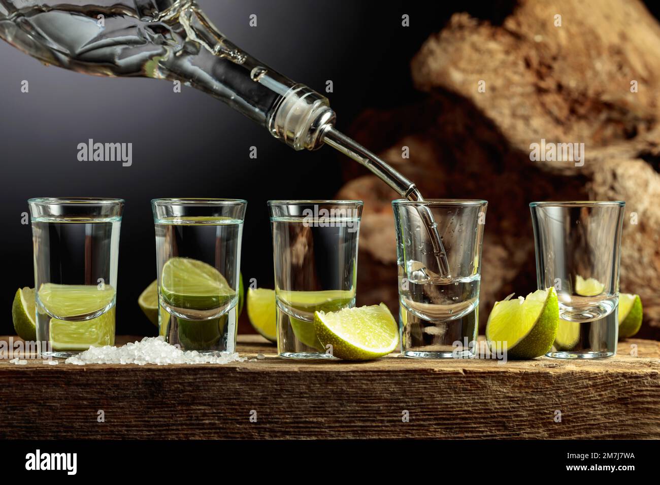 https://c8.alamy.com/comp/2M7J7WA/tequila-is-poured-from-a-bottle-into-a-glass-silver-tequila-with-salt-and-lime-slices-on-an-old-wooden-board-2M7J7WA.jpg