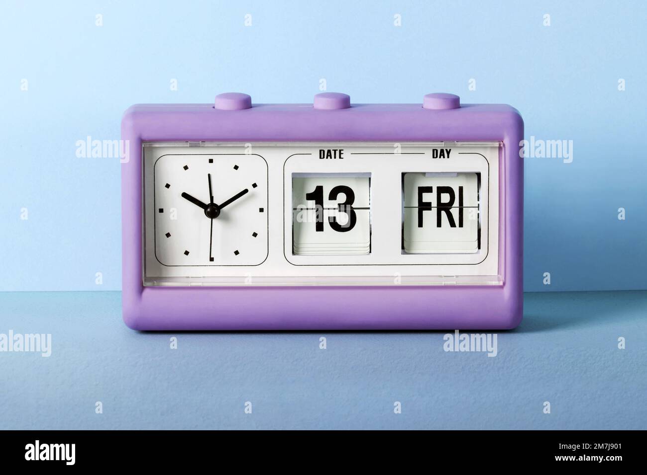 Violet alarm clock placed on table against blue wall set for Friday 13th Stock Photo