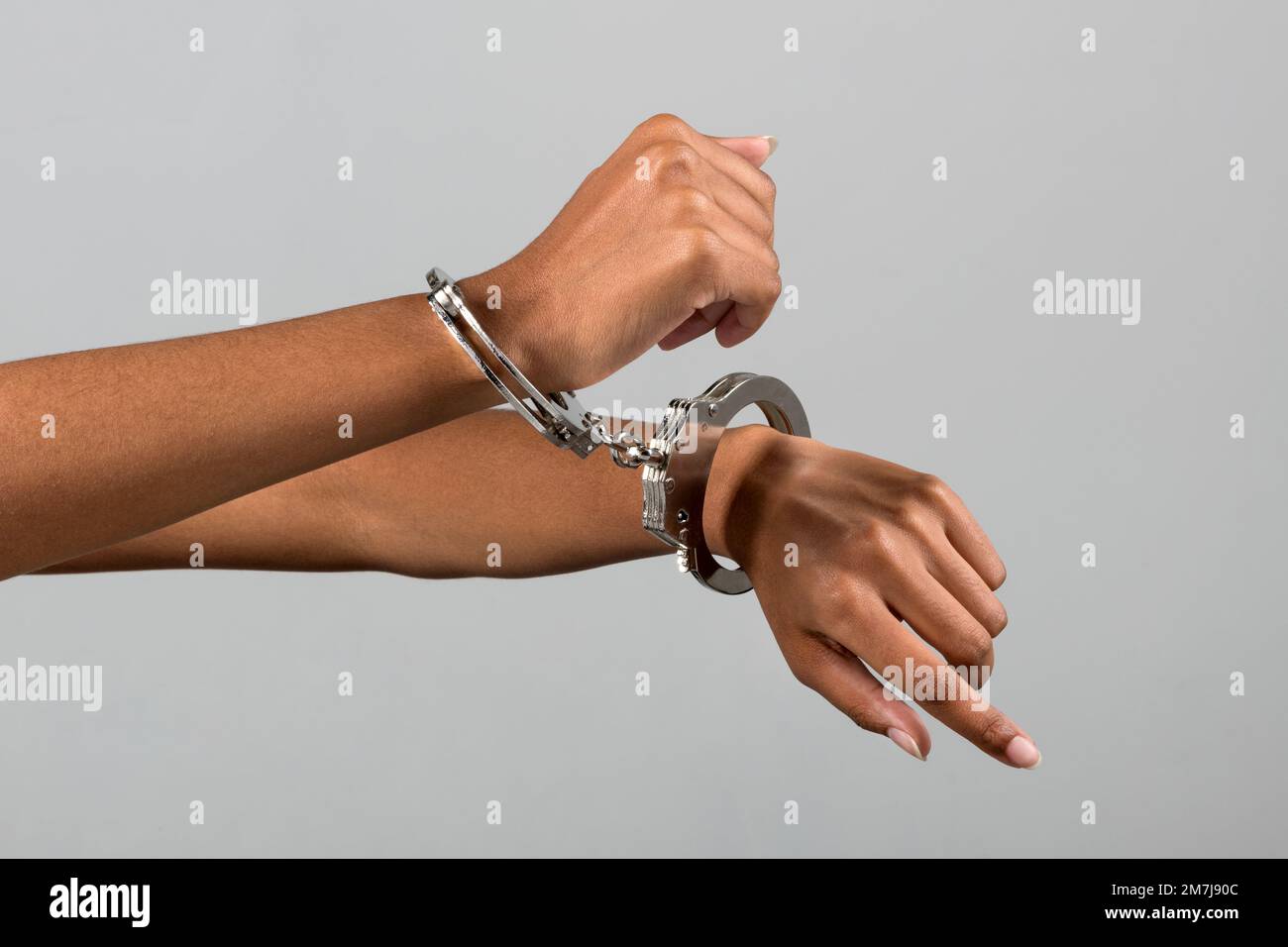 Anonymous African American female criminal trying to escape from handcuffs against gray background Stock Photo