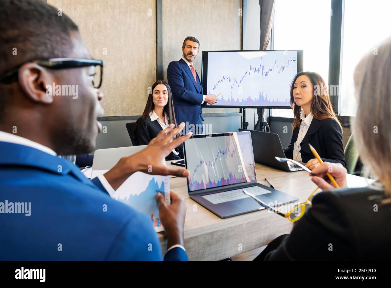 Group of multiethnic colleagues in formal wear gathering at table with laptops while discussing financial business project during presentation Stock Photo