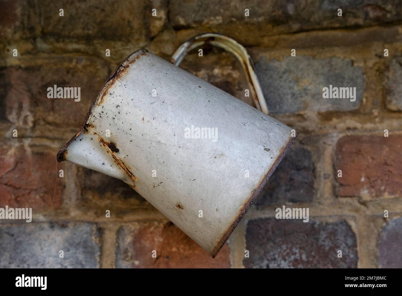 Old rusty enamel water jug hanging on a wall Stock Photo