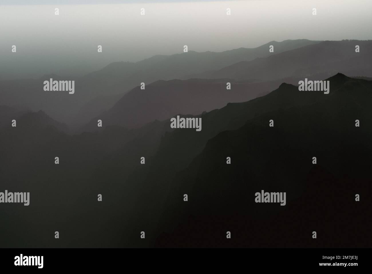 An aerial view of rocky mountains on a foggy day shot in grayscale ...