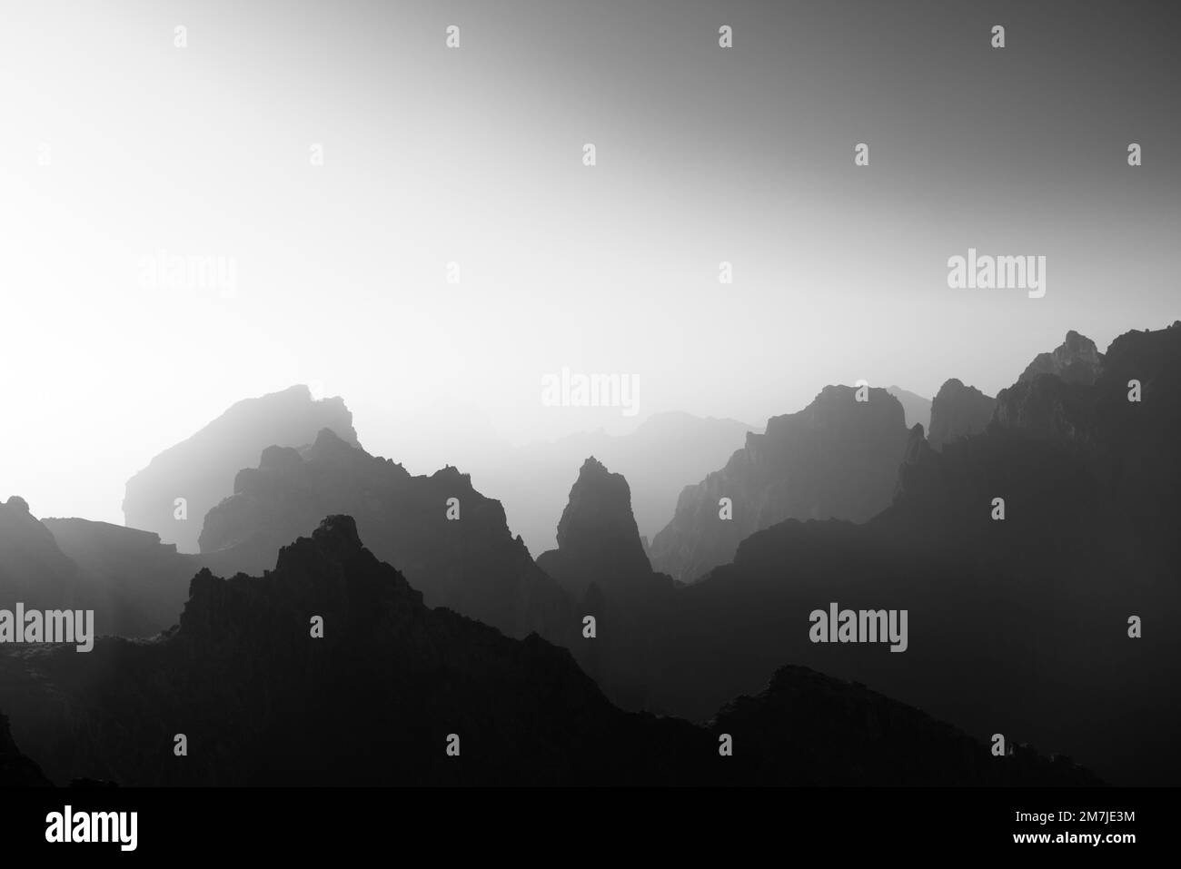 An aerial view of rocky mountains on a foggy day shot in grayscale ...